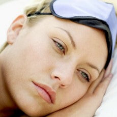 Women lying in bed in a pensive mood, wearing a sleep mask. Contemplating her poor sleep routine, due to her partners snoring. 
